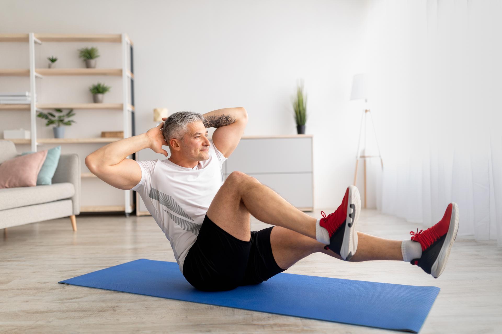 Sports during lockdown. Mature man doing home fitness on yoga mat, working out whole body at home